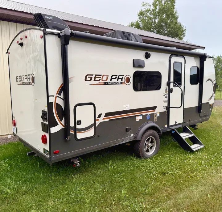 This Geo Pro by Rockwood travel trailer, ideal for an rv rental, is parked on grass. The compact RV has a white and brown exterior.. Forest River Rockwood Geo Pro 2025