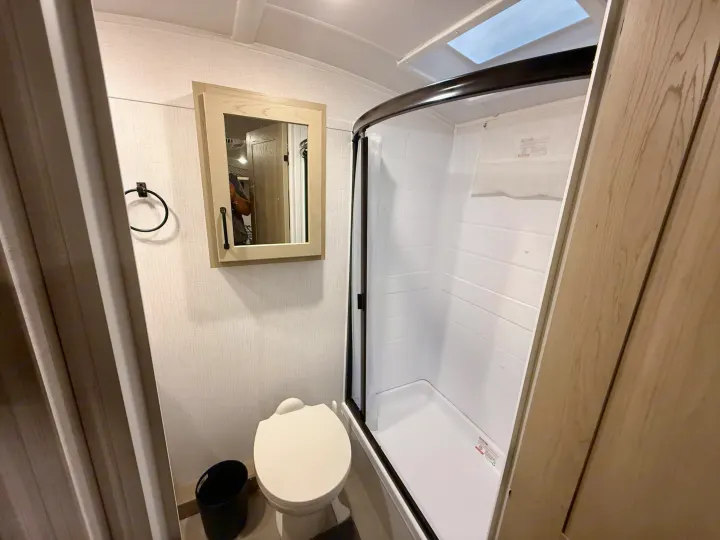This RV rental bathroom offers a compact design with a toilet, curved shower, and medicine cabinet with mirror.. Forest River Rockwood Geo Pro 2025