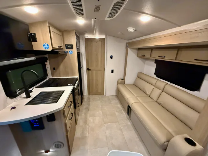 Spacious RV rental interior with a fully equipped kitchen (sink, stove) on the left, facing a comfortable cream-colored sofa.. Forest River Rockwood Geo Pro 2025