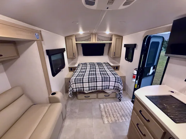 This compact RV rental interior features a comfortable bed, seating, and a small kitchen area, ideal for travel.. Forest River Rockwood Geo Pro 2025