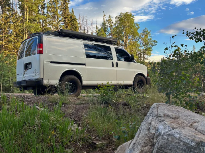 White camper van, ideal for RV rental adventures, parked by a forest with pines and aspens under a blue sky.. Chevrolet Express 1500 AWD 2007