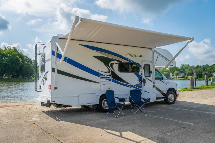 This Chateau RV rental with an extended awning and chairs offers a perfect lakeside retreat on a sunny day.. Thor Chateau 2023