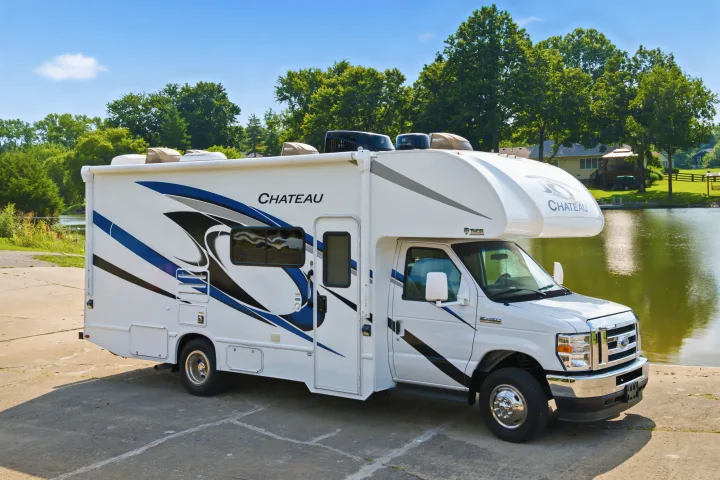 This white Thor Chateau Class C RV rental is parked by a lake, ready for your next adventure.. Thor Chateau 2023