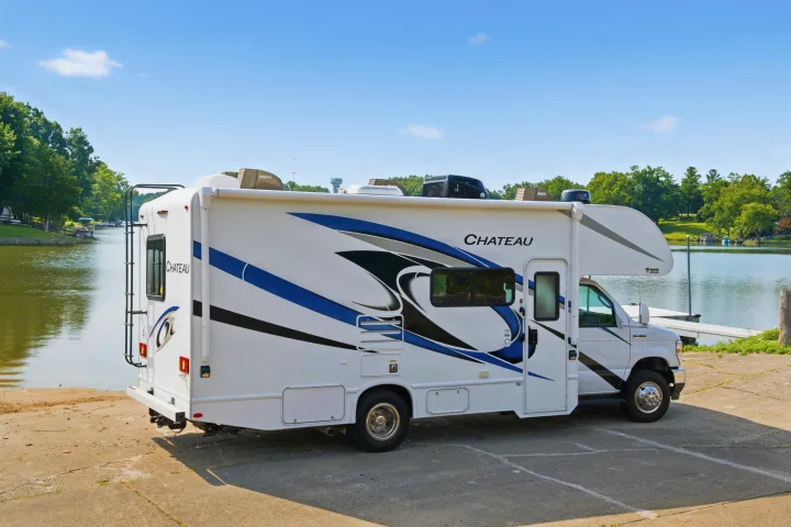 White Chateau Class C RV rental with blue accents, parked on a boat ramp next to a lake. Perfect for travel.. Thor Chateau 2023