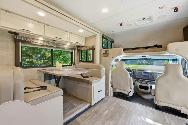 Inside a modern **rv rental**: bright dinette seating with safety belts, overhead cabinets, and the driver's area.. Thor Chateau 2023
