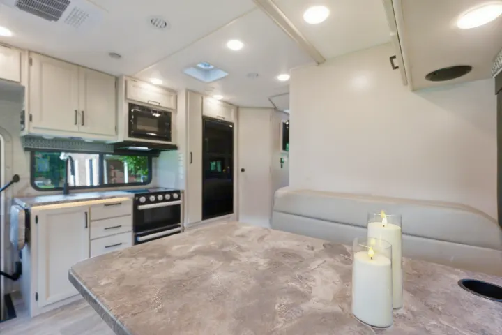 Bright and spacious RV rental interior, featuring a well-equipped kitchen, dining table with candles, and cozy dinette.. Thor Chateau 2023