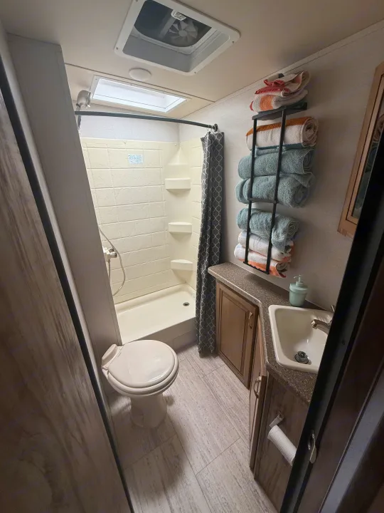 Compact RV rental bathroom with a shower, toilet, sink, and stacked towels on a wall-mounted rack.. Palomino Solaire 240BHS 2018