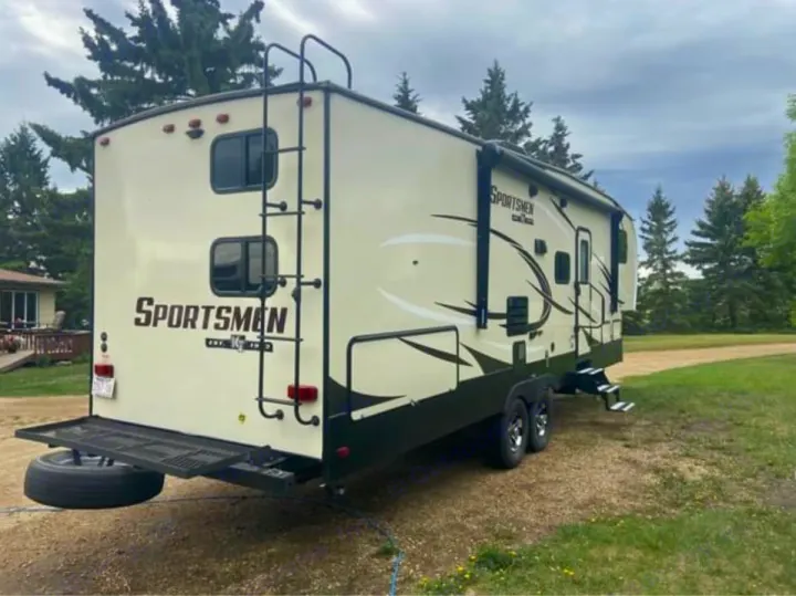 RV rental: Beige Sportsmen travel trailer with ladder, rear cargo rack, and awning, parked outside for adventure.. Sportsmen Sportsmen Fifth Wheel 2018