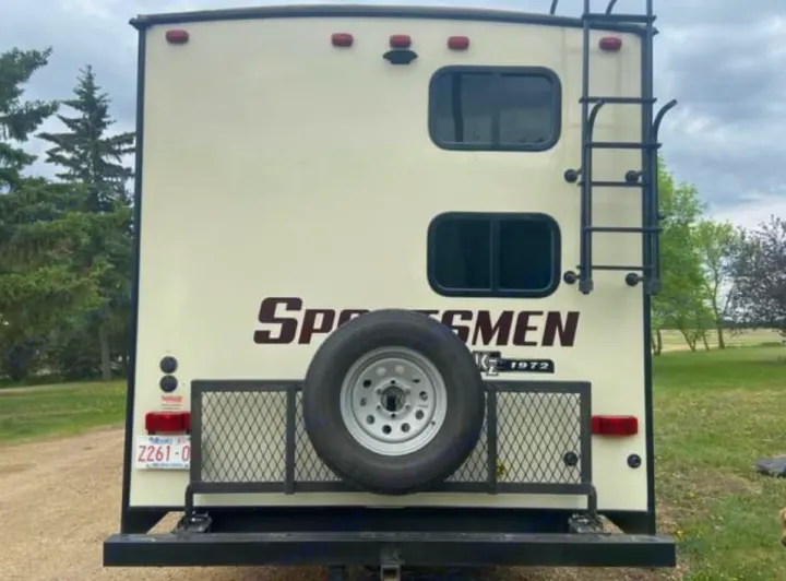 Rear of an RV rental showing a spare tire, ladder, two windows, and the "Sportsmen" logo, ready for your road trip.. Sportsmen Sportsmen Fifth Wheel 2018