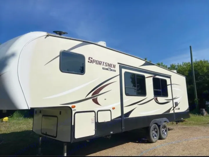 Tan & black 'Sportsmen' fifth-wheel RV rental, parked outdoors under a blue sky. Spacious camper for adventure awaits.. Sportsmen Sportsmen Fifth Wheel 2018