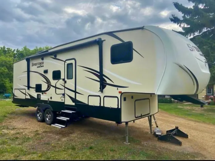 This cream fifth-wheel rv rental, featuring dual axles, an awning, and extended steps, is parked outdoors on jacks.. Sportsmen Sportsmen Fifth Wheel 2018