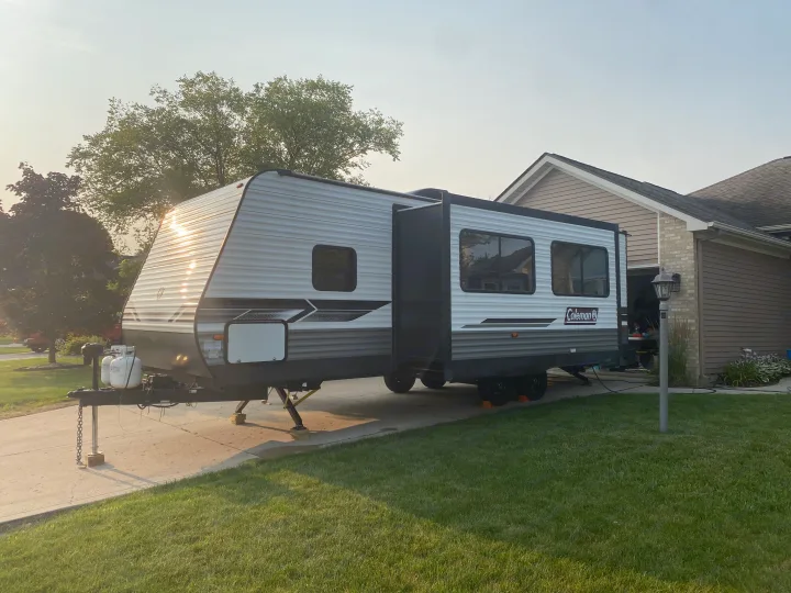 RV rental: A Coleman travel trailer is parked on a driveway by a house, slide-out extended & stabilizers set for camping.. Dutchmen Coleman Lantern LT 2022