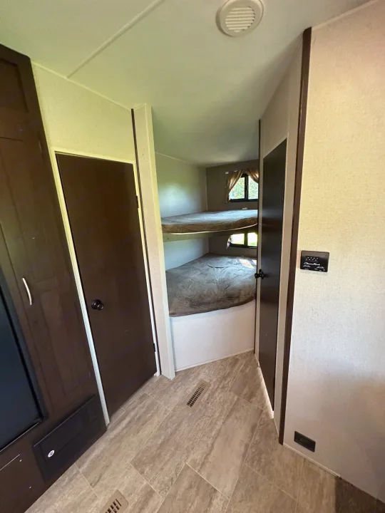 RV rental interior showing a compact bunk bed area, doors, and a control panel for comfortable travel.. Sportsmen Sportsmen Fifth Wheel 2018
