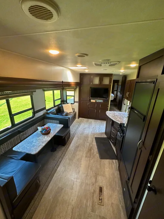 Inside a spacious rv rental, featuring a dinette, living area with couch, full kitchen, and stylish dark wood cabinets.. Sportsmen Sportsmen Fifth Wheel 2018