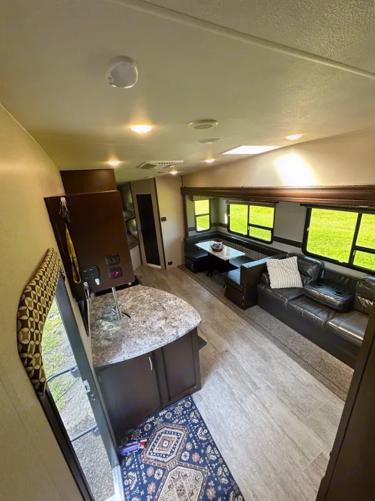 RV rental interior featuring a kitchen island, dining booth, and comfortable sofa with bright windows, showcasing a spacious living area.. Sportsmen Sportsmen Fifth Wheel 2018