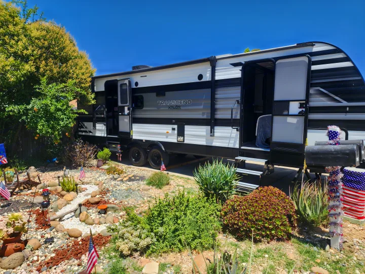 Transcend XPLÖR rv rental parked in a sunny yard with drought-tolerant landscaping & patriotic American flag decor.. Grand Design Transcend Xplor 2022