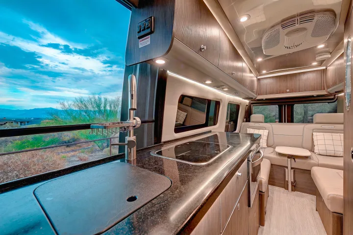 Inside a spacious RV rental: a modern kitchen, cozy lounge seating, and an expansive window with mountain views.. Airstream Interstate 2021