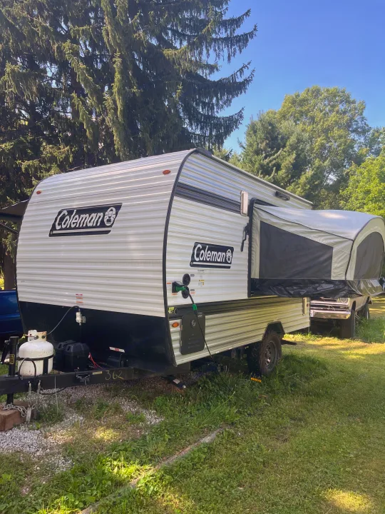 Coleman travel trailer rv rental with pop-out tent, parked on grass. Ready for outdoor adventures.. Keystone Coleman 13T 2026
