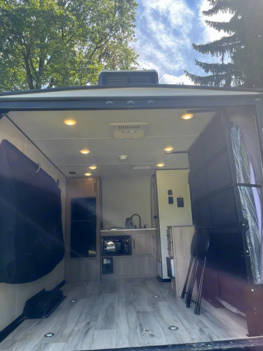 RV rental interior: A toy hauler with an open rear ramp, revealing a kitchen, fridge, bright ceiling lights, and tie-down floor.. Keystone Coleman 13T 2026