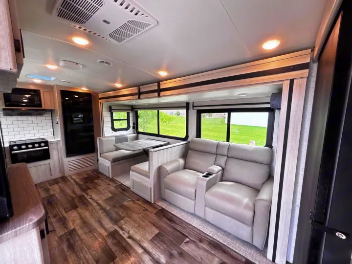 Bright rv rental interior: features comfy recliners, a dinette, kitchen, wood floors, and windows with green outdoor views.. Crossroads RV Sunset Trail Super Lite 2024