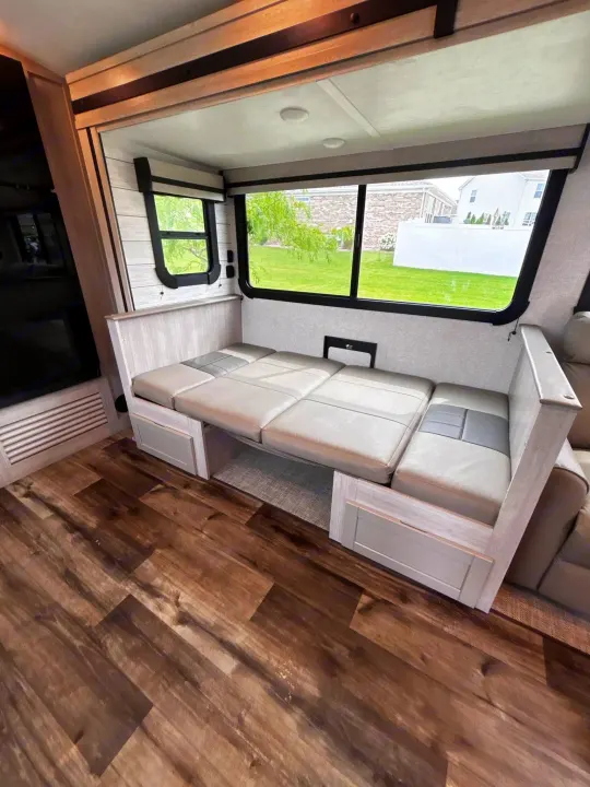 Cozy RV rental interior featuring a gray dinette that converts to a bed, wood-look flooring, and bright windows.. Crossroads RV Sunset Trail Super Lite 2024