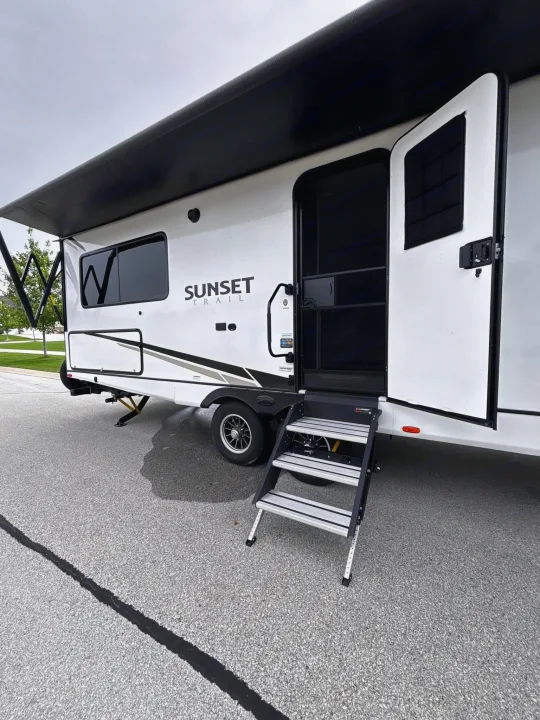 Side view of a white Sunset Trail travel trailer rv rental, with door open and steps extended for easy entry.. Crossroads RV Sunset Trail Super Lite 2024