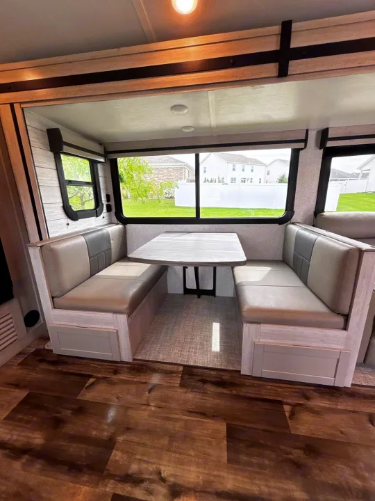 Modern **RV rental** dinette interior with light gray benches, a table, and large windows showing a suburban view.. Crossroads RV Sunset Trail Super Lite 2024