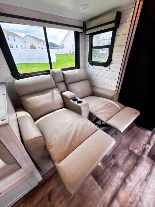 Relax in this RV rental's cozy interior with plush recliners, cup holders, and a bright window showing a neighborhood view.. Crossroads RV Sunset Trail Super Lite 2024