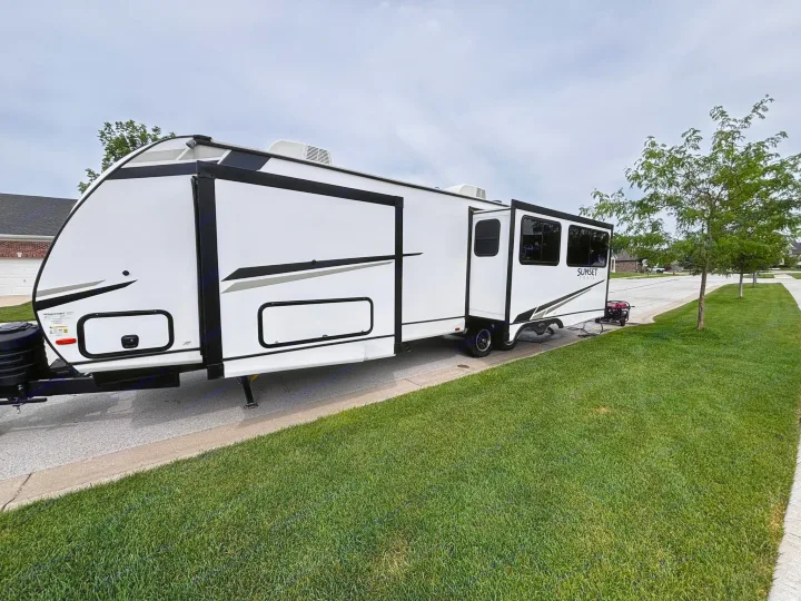 This modern white travel trailer RV rental, with multiple windows and a generator, is parked on a residential street.. Crossroads RV Sunset Trail Super Lite 2024