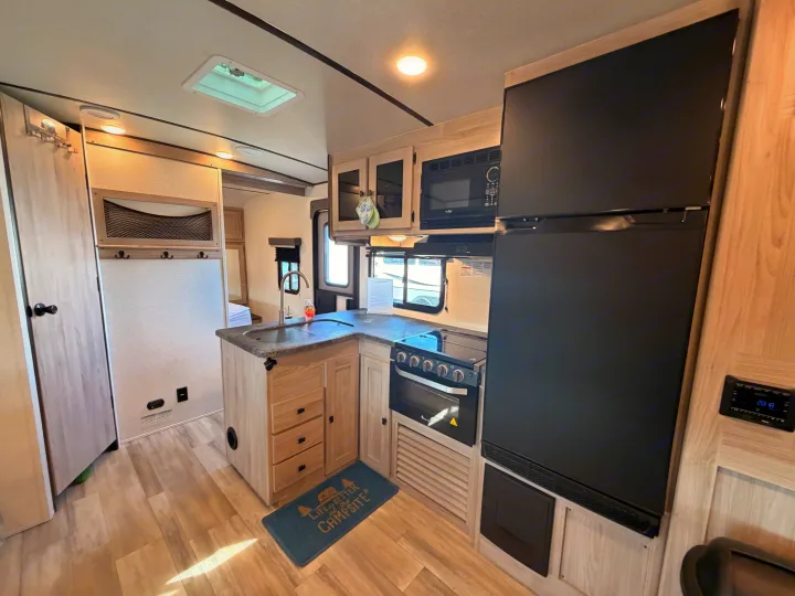 A bright, modern rv rental kitchen featuring a large fridge, stove, microwave, sink, ample cabinets, and wood-look flooring.. Coachmen 2963BH 2023