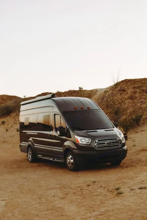 Dark Ford Transit rv rental camper van, equipped with an awning, parked on a dirt road in a desert landscape. Ideal for adventure.. Forest River Coachmen Crossfit 2018