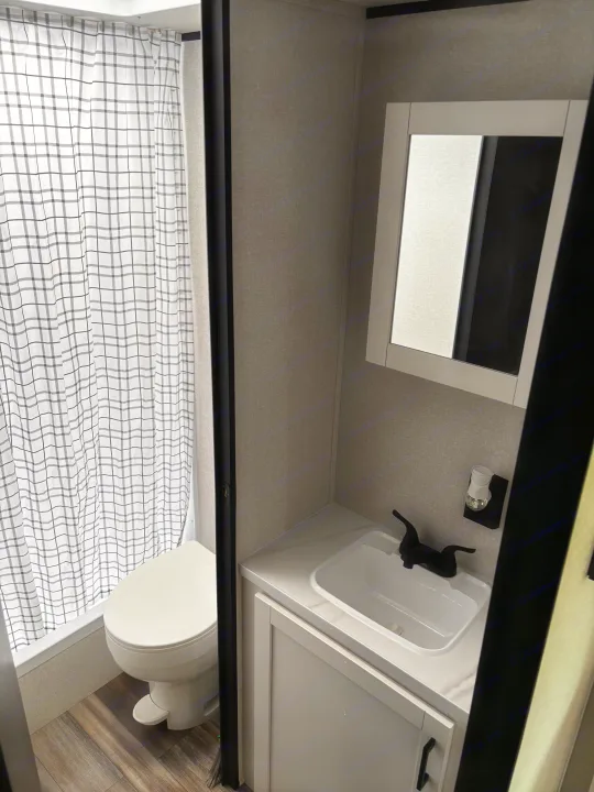 This modern RV rental bathroom features a toilet, plaid shower curtain, sink, and mirrored medicine cabinet.. Starcraft Autumn Ridge 2026