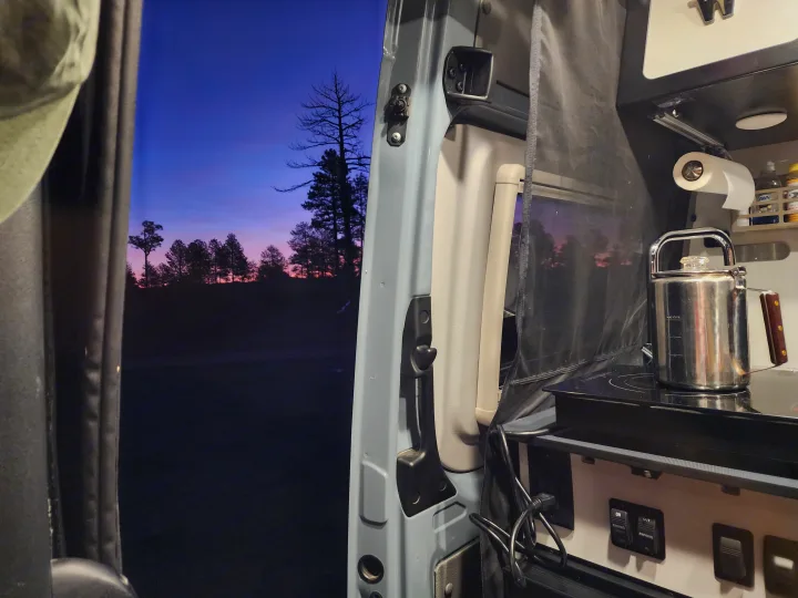 A vibrant twilight sky with silhouetted trees seen from an rv rental camper van, featuring a cozy kitchenette with a percolator.. Winnebago Revel 2021