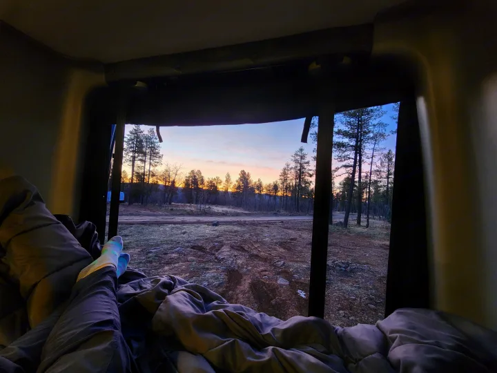 Peaceful rv rental morning. View from a cozy bed reveals a beautiful forest sunrise over a dirt path, perfect for camping.. Winnebago Revel 2021