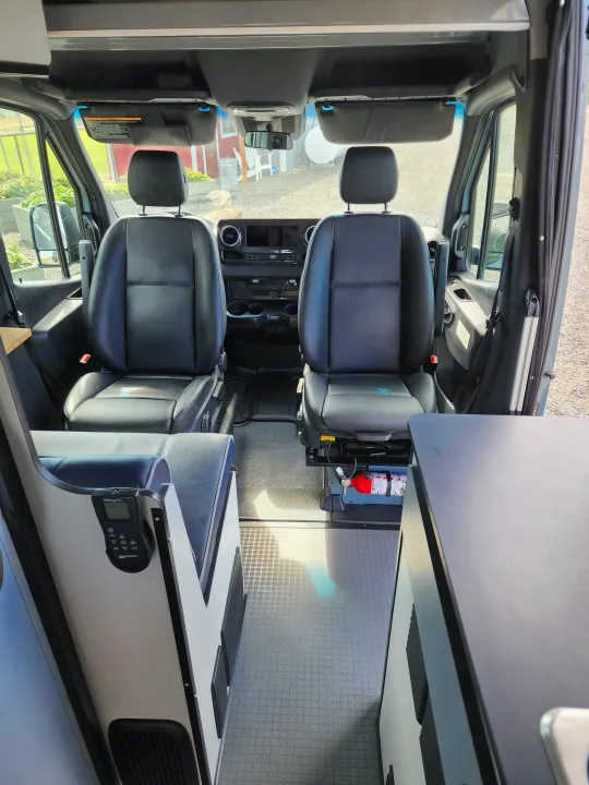 RV rental interior: front cockpit view with black seats, dashboard, rubber floor, and essential controls/fire extinguisher.. Winnebago Revel 2021