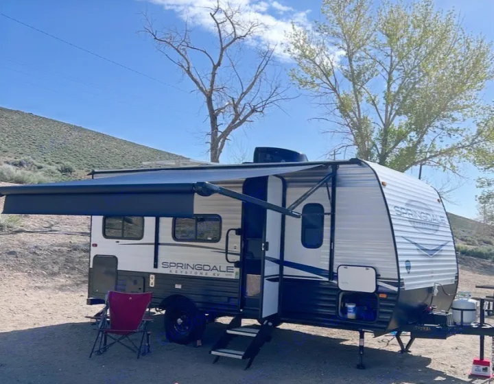 This Springdale RV rental is set up at a scenic campsite with its awning extended, perfect for your next outdoor adventure.. Keystone RV Springdale 2023