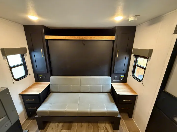 RV rental interior: a grey convertible sofa, dark overhead cabinets, and small side windows. Functional space for travelers.. Keystone RV Springdale 2023