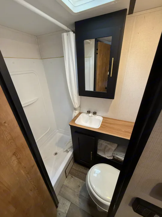 This RV rental's modern bathroom features a white shower, toilet, and black vanity with a mirror cabinet.. Keystone RV Springdale 2023