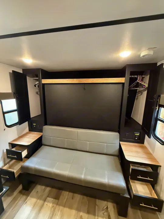 Modern RV rental interior featuring a gray sofa, murphy bed, built-in storage, and side tables. Ideal for compact living.. Keystone RV Springdale 2023