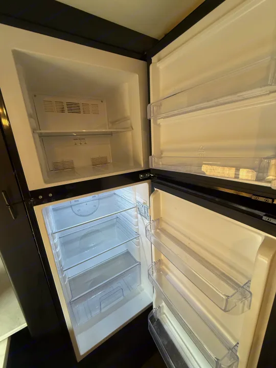 This clean, empty RV rental refrigerator and freezer with open doors and clear shelves is ready for your trip's provisions.. Keystone RV Springdale 2023