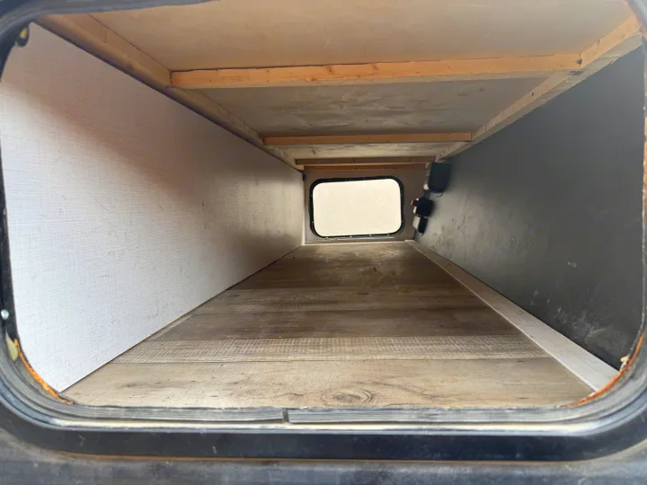 Interior of RV rental storage: wood-look floor, light & dark walls, back window, & fixtures.. Keystone RV Springdale 2023