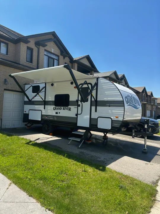 Grand River rv rental: A white travel trailer with an extended awning is parked in a driveway, ready for your next adventure or road trip.. Gulf Stream Grand River 2024