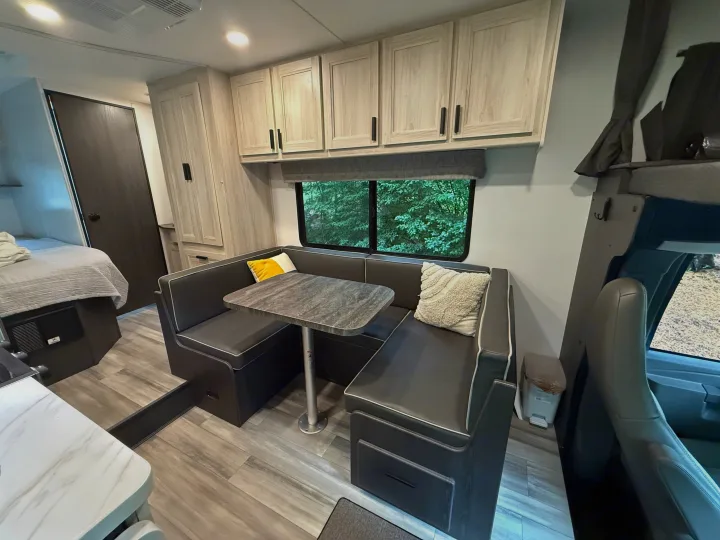 Cozy RV rental interior featuring a dinette with bench seating, overhead cabinets, and a window view of green trees.. Forest River Sunseeker LE 2023