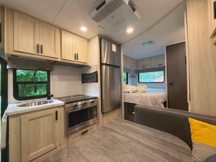 Modern rv rental interior: light wood kitchen with stainless steel appliances, dining booth, and bedroom with a comfy bed.. Forest River Sunseeker LE 2023