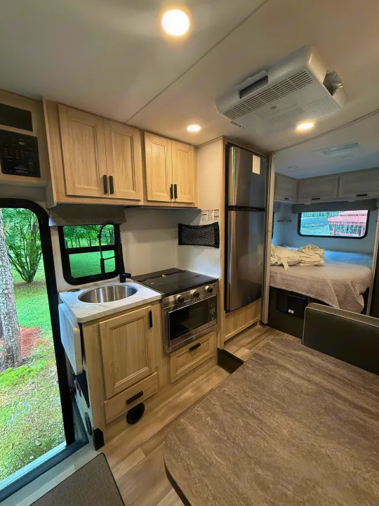 Bright RV rental interior with kitchen, dining, and bedroom areas, showcasing light wood accents and a view of nature.. Forest River Sunseeker LE 2023