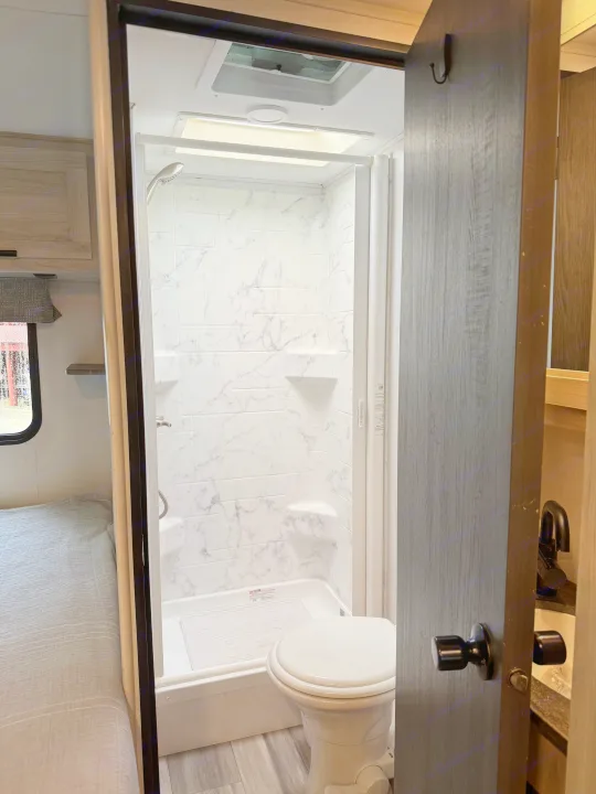 Compact RV rental bathroom with shower, toilet, and adjacent bedroom area.. Forest River Sunseeker LE 2023