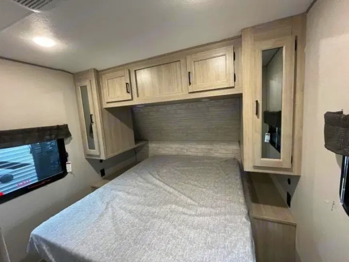 Explore this RV rental's cozy bedroom featuring a comfy bed, compact overhead cabinets, and a window for light.. Forest River Catalina Coachmen Legacy 293QBCKLE 2026