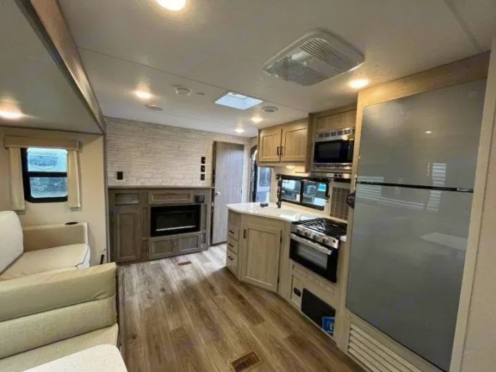 Modern rv rental interior features a full kitchen with fridge, stove, and microwave, plus a cozy living area with sofa and fireplace.. Forest River Catalina Coachmen Legacy 293QBCKLE 2026