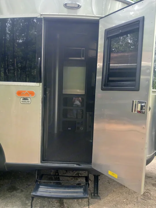 A silver Airstream travel trailer rv rental with its main door open, revealing the screen door, interior, and deployed steps.. Airstream Basecamp 2022