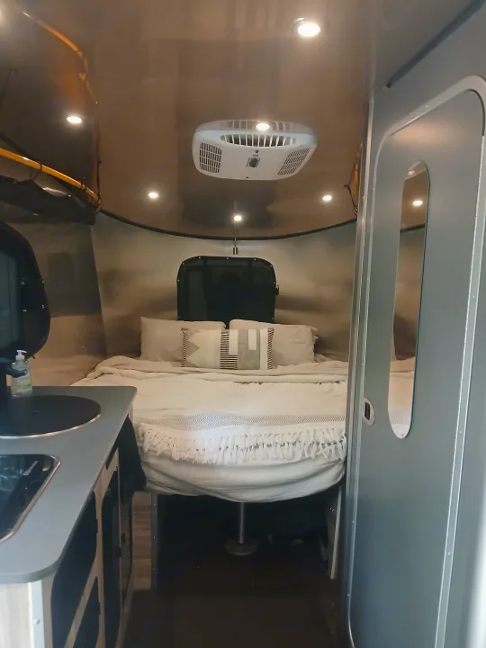 Cozy interior of an **rv rental** showing a comfortable bed, overhead AC unit, and a compact kitchen counter. Ideal for travel.. Airstream Basecamp 2022